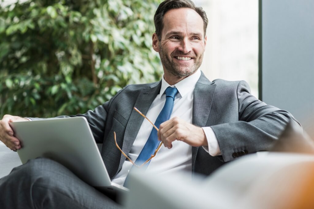 Retrato de um empresário sorridente sentado no saguão com um laptop.